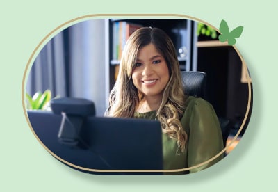 foto da psicóloga Bruna Monteiro sorrindo sentada à frente de um computador com webcam